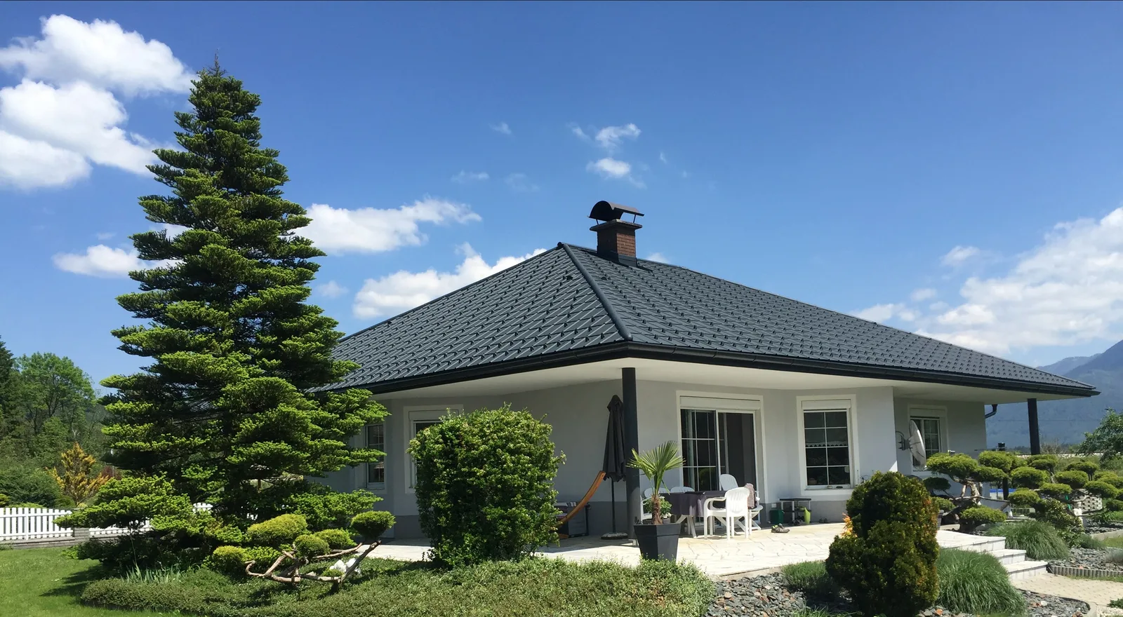 Bungalow mit anthrazitfarbenem Dachplattendach vor Bergpanorama