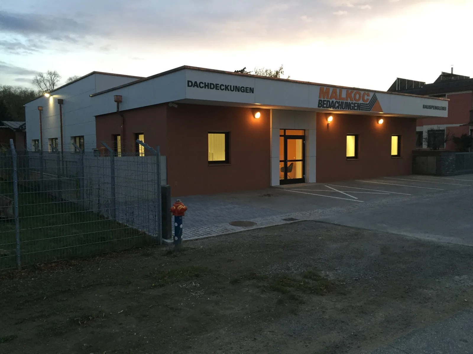 Betriebsgebäude von Malkoc Bedachungen am Abend, das Firmenschild ist beleuchtet