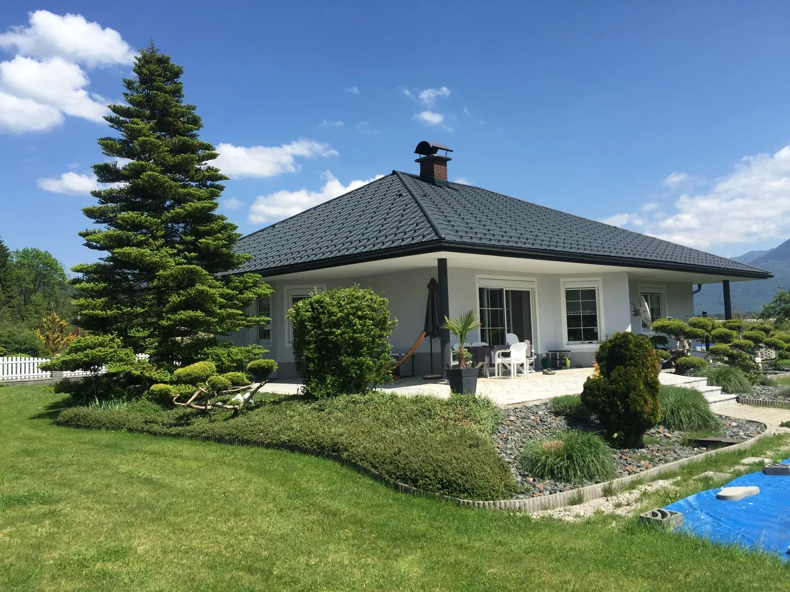 Bungalow mit anthrazitfarbenem Walmdach, Garten im Vordergrund