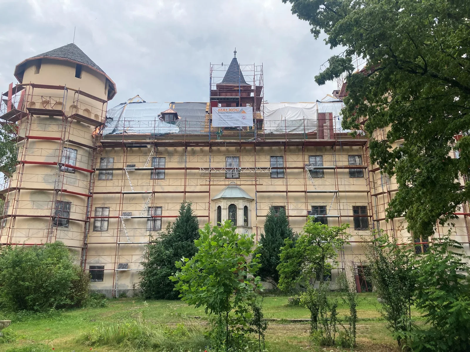 Eingerüstete Schlossanlage, auf dem Gerüst hängt eine Plane mit dem Schriftzug Malkoc Bedachungen